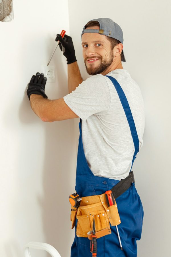 Enthusiastic electrician, handyman looking at camera with a smile while working on wiring in new