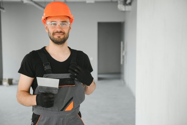 Tradesman on stilts plastering drywall in home