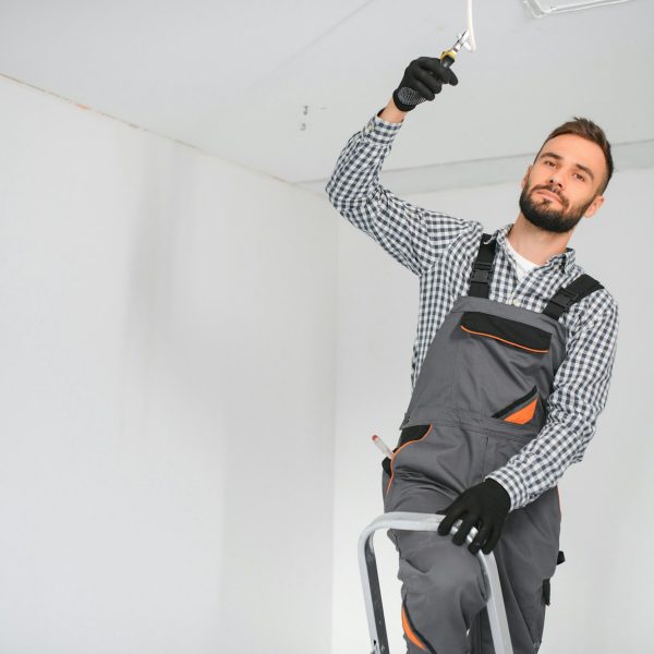 Young electrician installing smoke detector on ceiling.